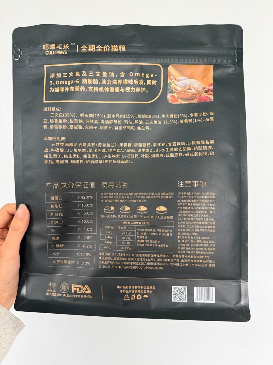 咕噜毛孩三文鱼款包装背面实拍：原料组成与添加剂组成、产品成分保证值（粗蛋白 ≥ 42.0%）、七日换粮过渡与每日建议喂食量表